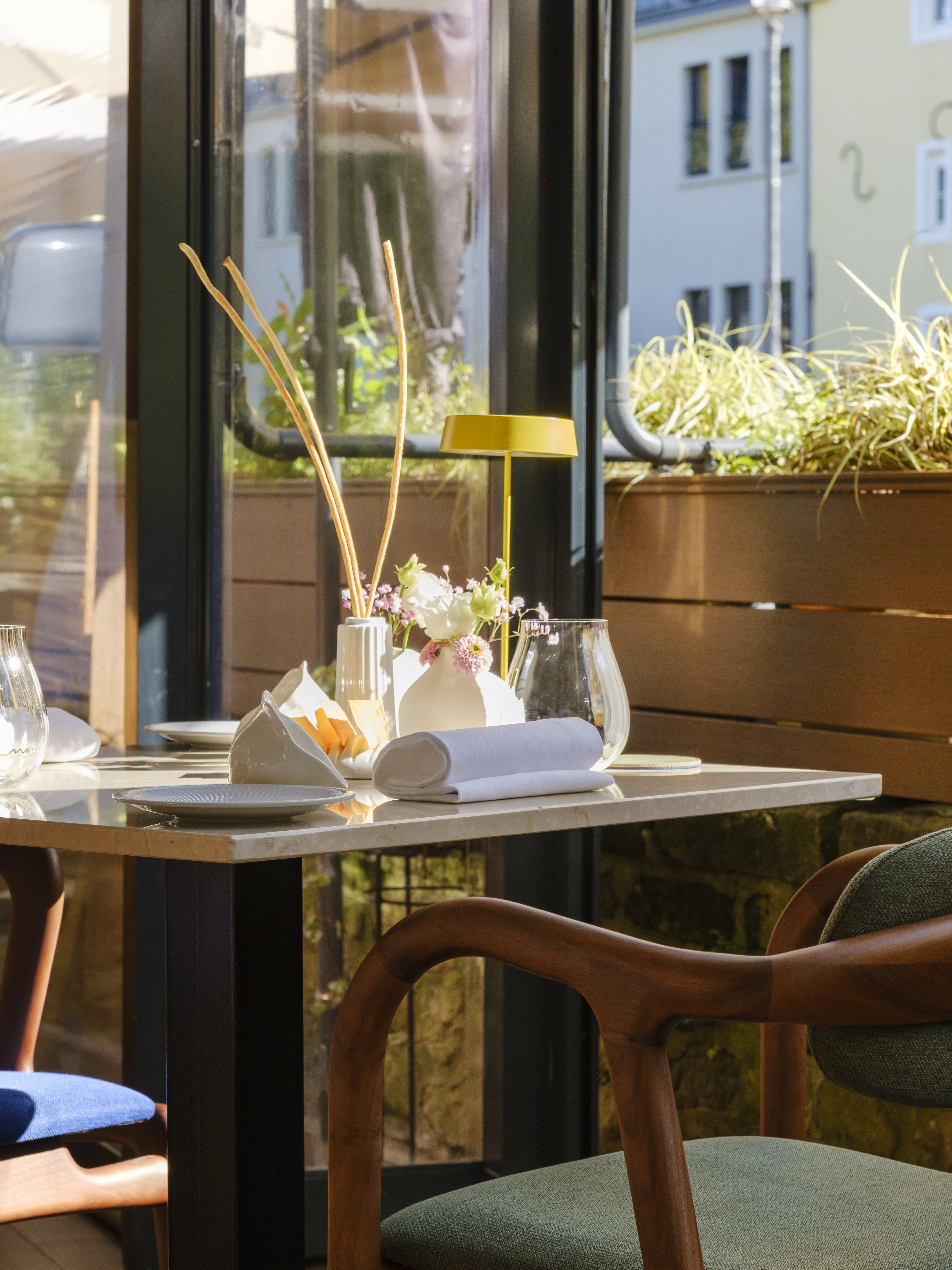 A terrace table at OiO laid with flowers, a folded napkin and a brass lamp, houses beyond the rail