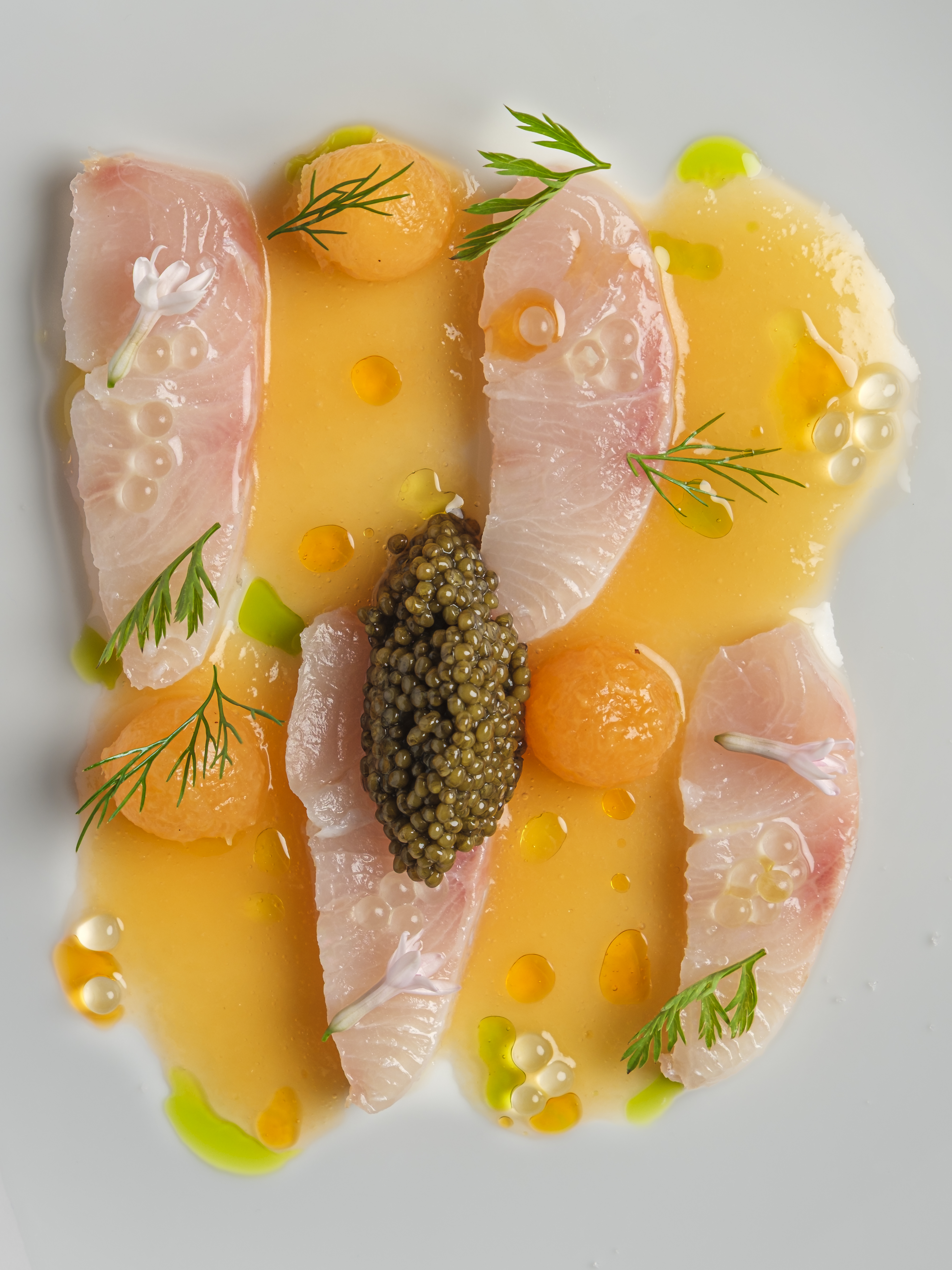 Yellowtail crudo with melon, citrus and oscietra caviar on a white plate