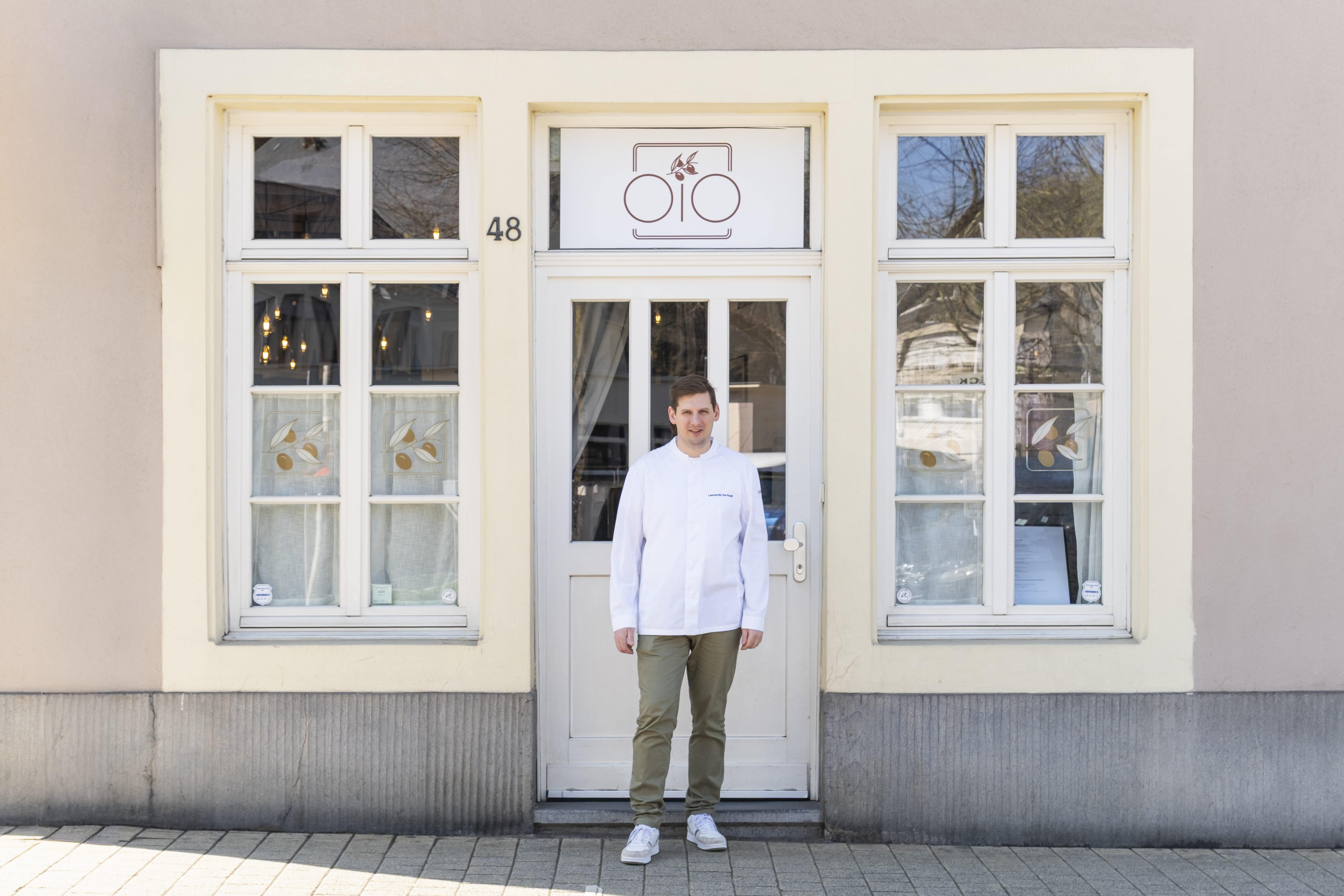 Leonardo De Paoli in his whites at the door of number 48, Montée de Clausen, under the OiO sign