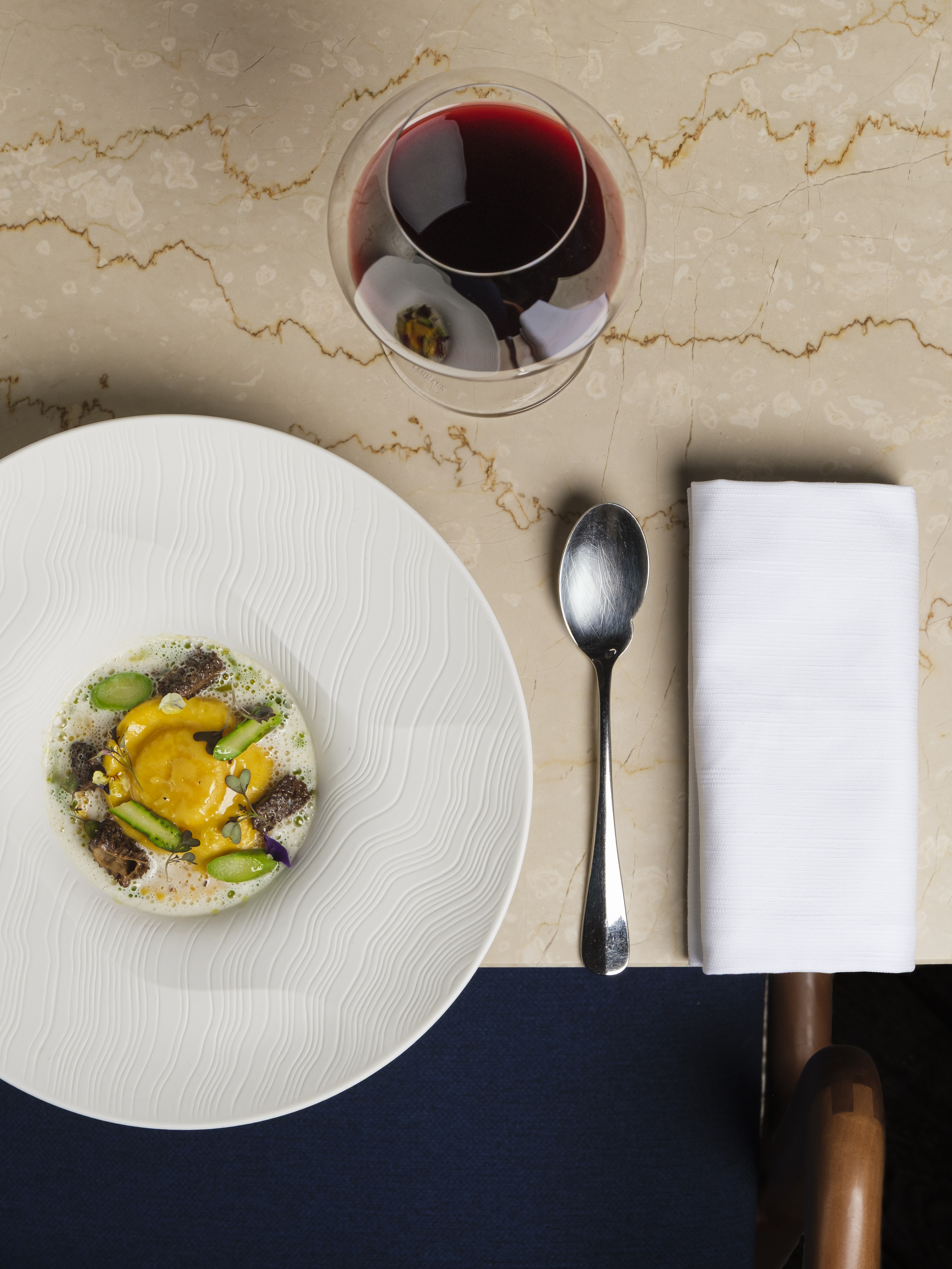 A plated first course beside a glass of red wine and a folded napkin on cream marble
