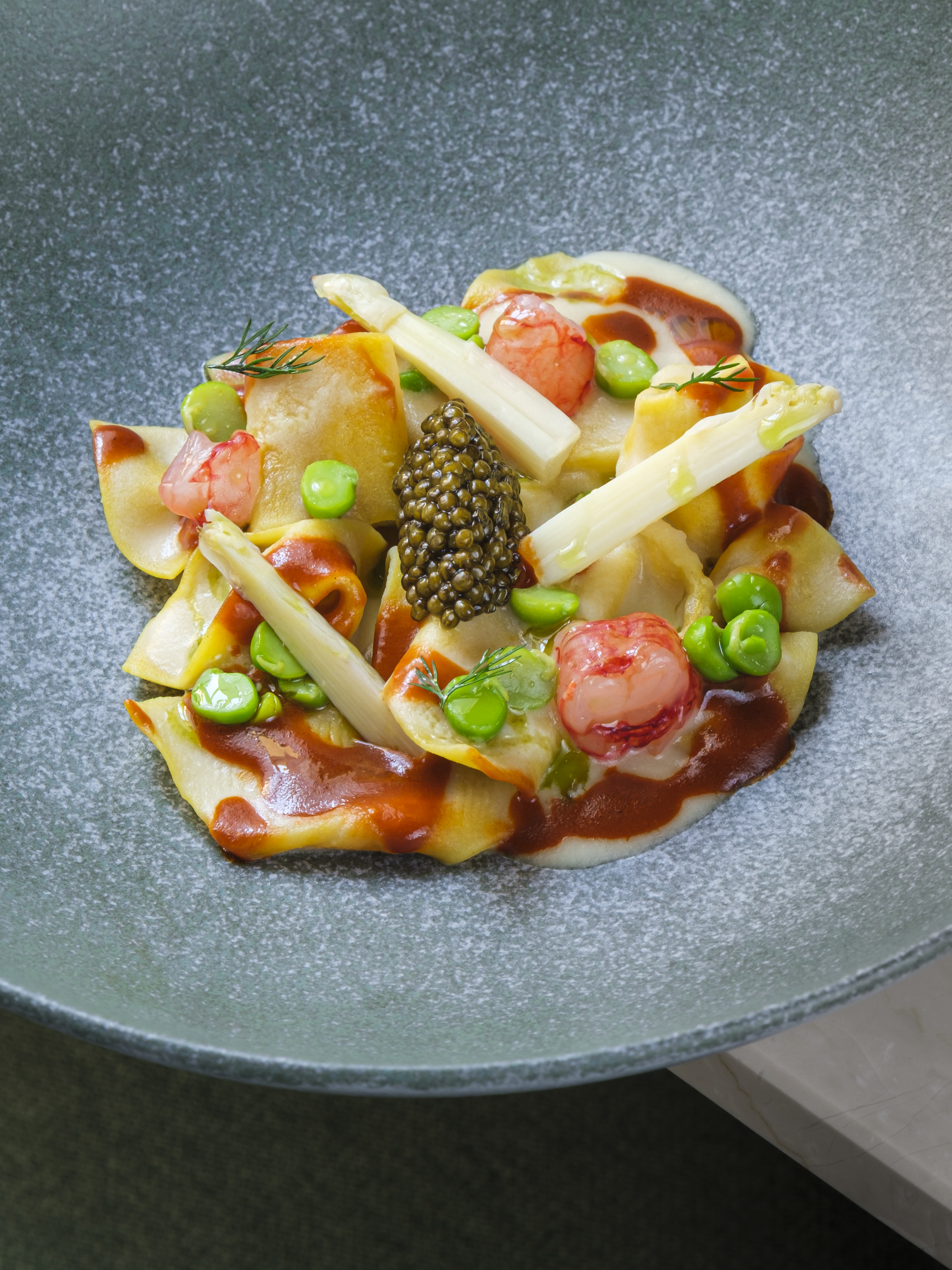 Pasta with caviar, broad beans and tomato on a green stoneware plate